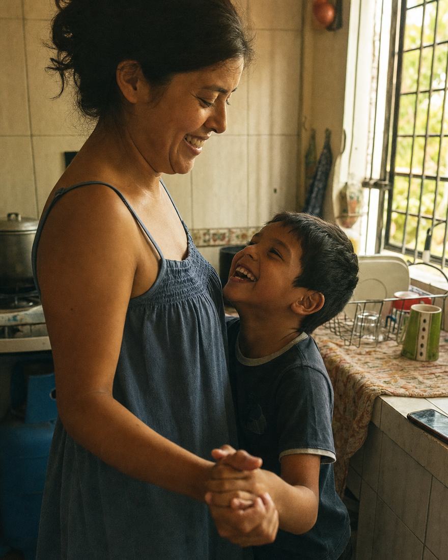 Una madre baila descalza en la cocina con su hijo pequeño, los dos riendo, con el celular apoyado en la encimera